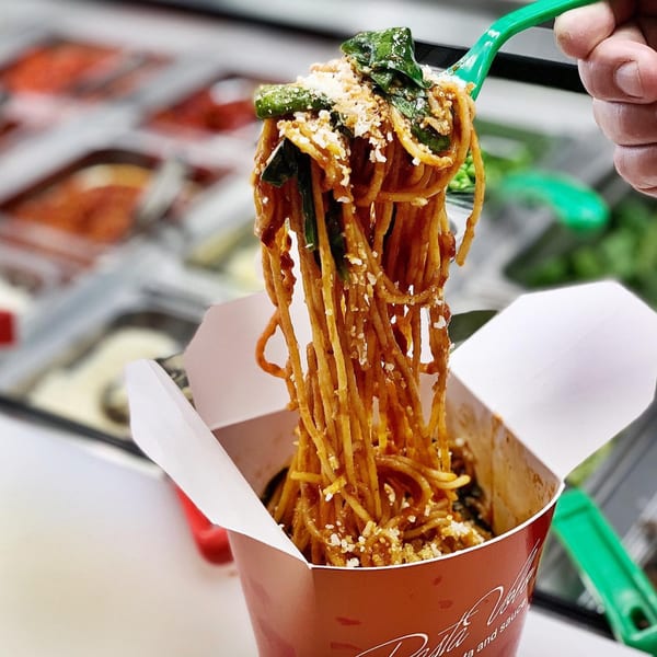 A green fork lifts saucy Pasta Volo spaghetti with spinach and cheese from a takeout box.