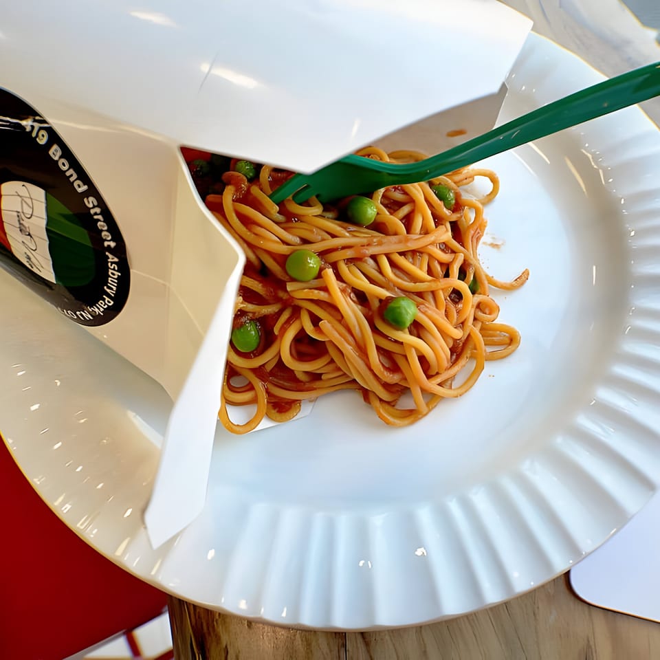 Pasta Volo's spaghetti with peas and red sauce, served in a takeout box on a white plate.