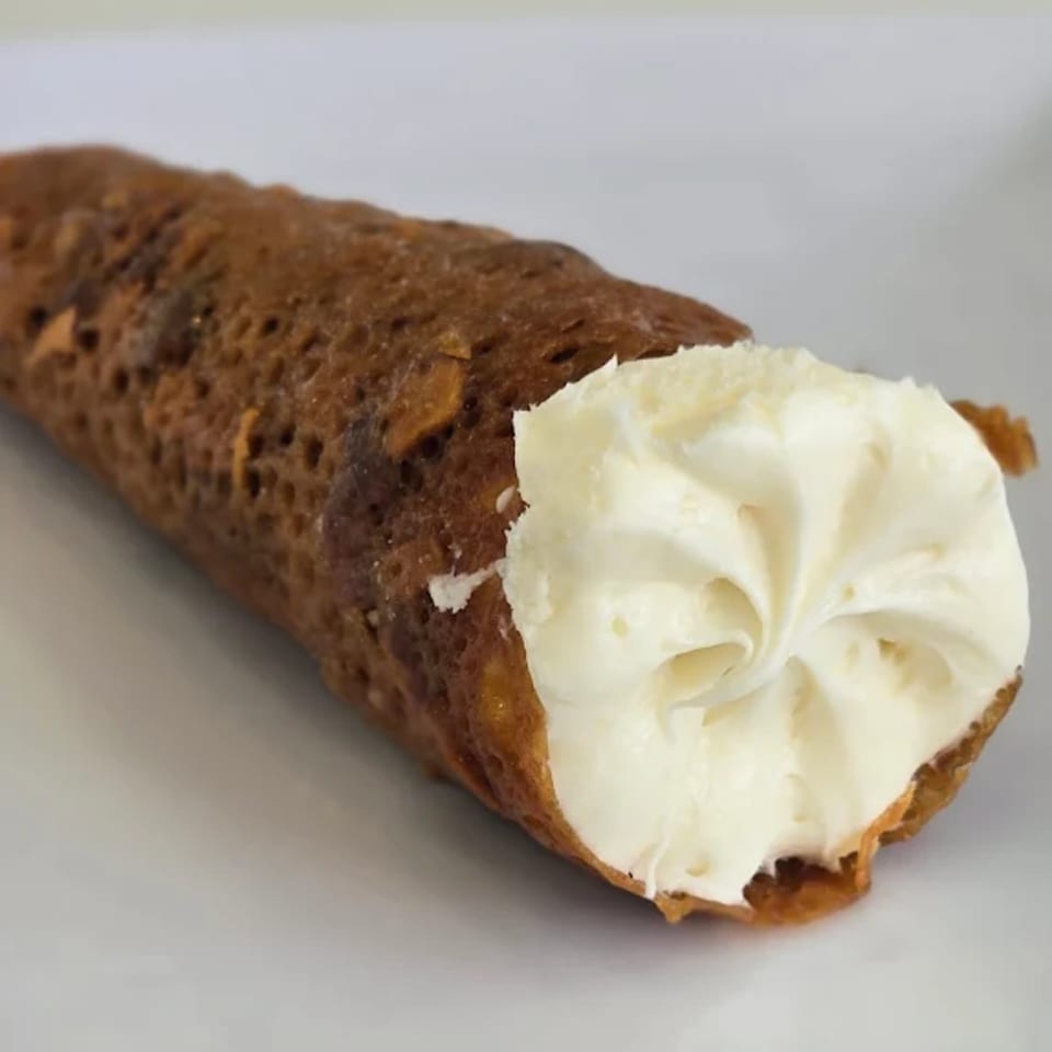 A close-up of a golden-brown cannoli shell generously filled with creamy white ricotta cheese.