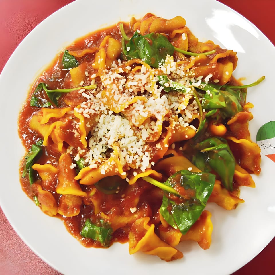 Pasta Volo's tortellini with tomato sauce, fresh spinach, and grated cheese on a white plate.