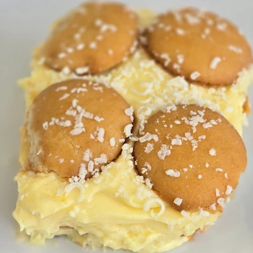 Banana pudding dessert with vanilla wafers and white chocolate shavings on a white plate.